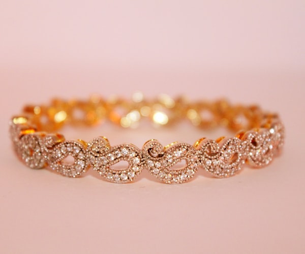 Rose gold infinity-link bracelet with pavé diamonds on a blush pink background