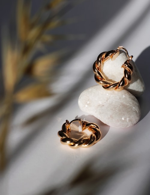 Twisted gold hoop earrings styled on white stones with natural shadow accents